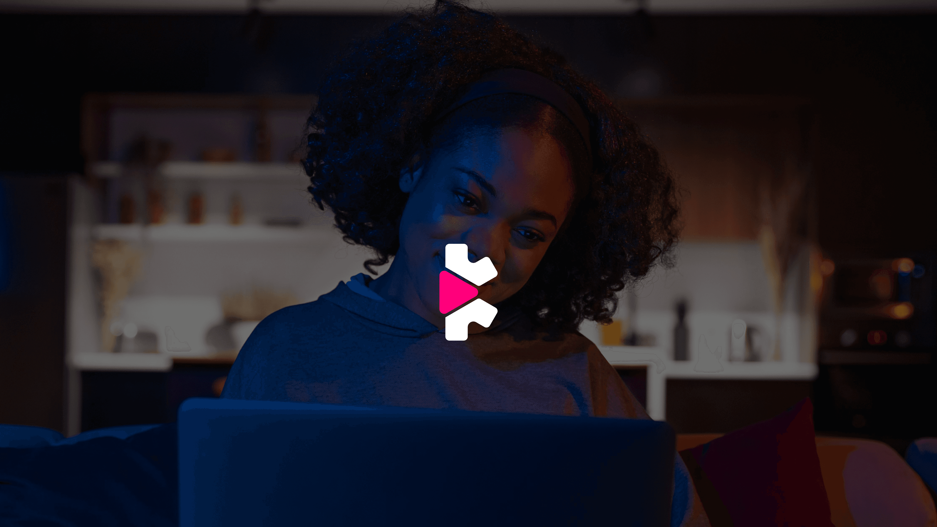 A woman smiling at her laptop screen at night, with the SyncWatch logo mark overlaid in the center of the frame